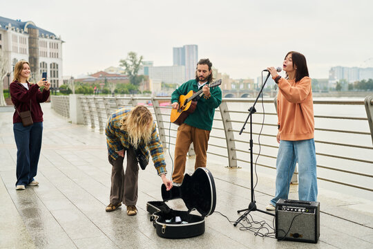 Group of young adults performing live music outdoors, Caucasian man playing guitar, young woman singing into microphone