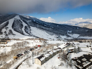 Naklejka premium Aerial drone view of Madarao ski resort with snowy slopes and village in Nagano, Japan