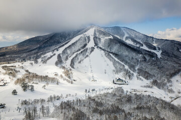 Obraz premium Wide shot of snow-covered ski slopes, chairlifts, and forests at a Japanese resort