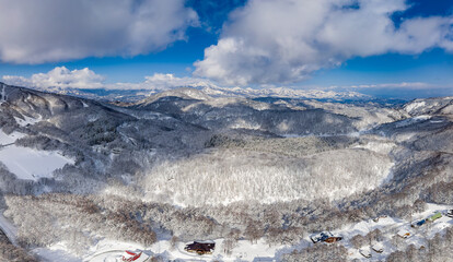 Aerial drone view of snow-covered mountains and forests in Madarao, Japan.