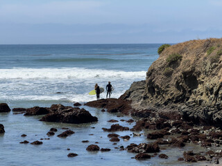 Silhouette of two surfers in wetsuits looking to jump in the water, but checking the waves first.