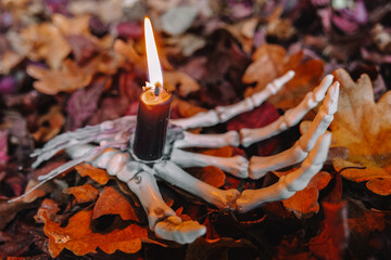 Spooky Halloween Candlestick.Skeleton Hand Holding Candle in Autumn Leaves. halloween candle. 