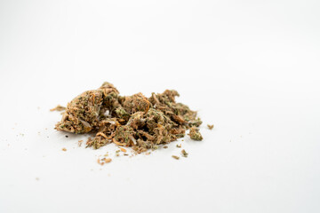 Pile of dried cannabis buds is spread out on white surface, showcasing the texture and appearance of the plant material. Selective focus