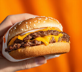 Hand Holding Double Cheeseburger with Melted Cheese on Orange Background