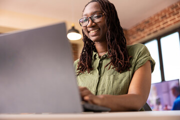 Cheerful woman entrepreneur using laptop at home, reviewing company finances and researching...