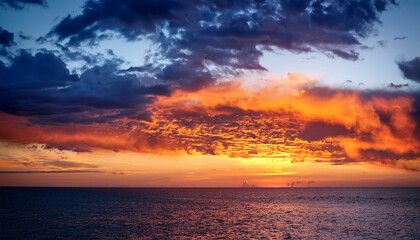 Fototapeta premium a fiery sunset paints the dramatic cloudscape with hues of orange and blue casting long shadows on the tranquil sea