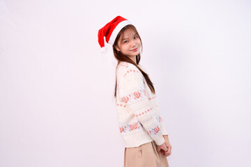 smiling pretty young woman wearing santa hat and festive cardigan for christmas in white studio...