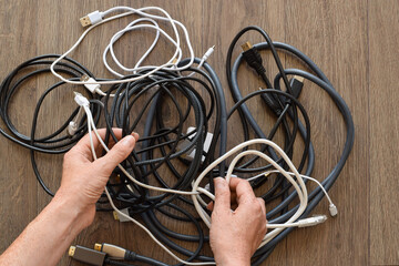 Closeup of woman’s hands organizing a pile of assorted cables and cords. Concept of technology clutter, electronic organization, recycling, and modern lifestyle