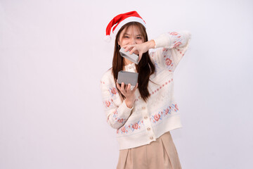 young pretty woman celebrating christmas holding a mini gift box and looking cheerful with santa head in white studio background