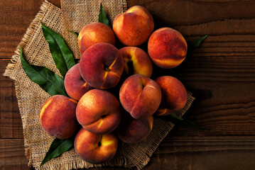 Hig angle shot of a large group of Yellow Cling Peaches on burlap and dark wooden boards.