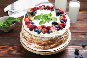 Delicious crepe cake with fresh berries and milk on wooden table, closeup