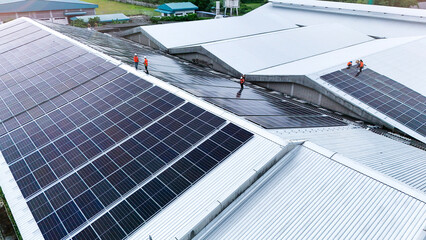 erial drone view of workers installing solar panels on a factory rooftop. The team is building a...