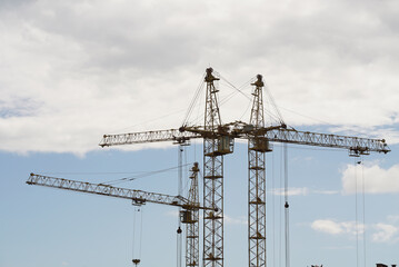 The image of construction cranes rises against a backdrop of a beautifully cloudy sky. Majestic cranes at a bustling site under a dynamic sky, symbolizing the rapid pace of urban developmenty