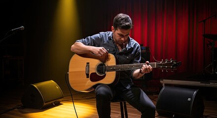 Obraz premium A man playing an acoustic guitar in a dimly lit room with a red curtain in the background.