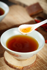 Golden honey dripping from spoon into brown ginger tea bowl on wooden table