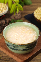 Traditional rice porridge in ceramic bowl on wooden base with buckwheat grains and herbs