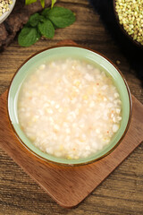 Homemade Rice Porridge in Green Bowl on Wooden Board with Fresh Mint and Buckwheat Grains