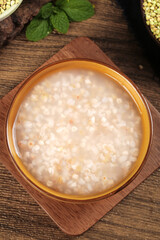 Homemade rice porridge in ceramic bowl on wooden board with mint and buckwheat grains
