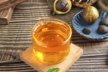 Camellia Seed Oil in Glass Cup with Fresh Camellia Fruits on Rustic Wood Table
