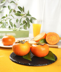 Fresh Persimmons on Slate Plate with Orange Juice Glass White Background