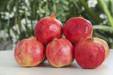 Fresh Red Pomegranates on White Surface with Green Natural Background