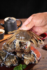 Fresh Taihu hairy crab held by hand closeup with tea - delicious Chinese seafood delicacy on wooden table bottom view