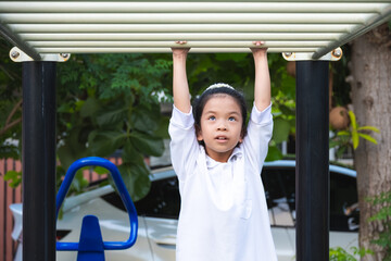 Obraz premium Portrait of Happy girl swinging on the monkey bars in playground. Exercise for health of 8-9 year old Asian girls.