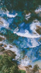 Obraz premium An aerial view captures turquoise ocean waves crashing against dark rocks, meeting a sandy shore fringed with lush green vegetation