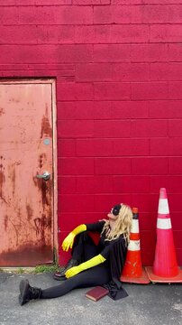 A super hero woman is sitting down on the ground of a building and looks tired or bored for an energy, focus or confidence concept.