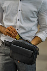 A man's hand in a white shirt is putting a smartphone into a black leather handbag.