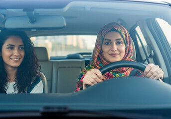 Happy Arab woman wearing a hijab confidently driving her car with a female friend as a passenger on a sunny day