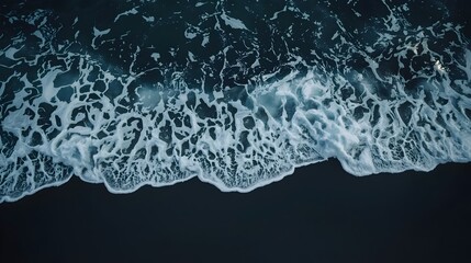 "Ocean waves crashing on dark sandy beach, sea foam patterns forming along shoreline, deep blue water and white surf creating natural textures, peaceful seascape and coastal background"