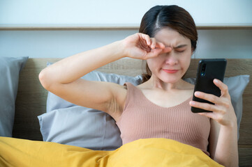 Asian woman feel sleepy while playing and surfing internet on her smartphone. Insomnia people and mobile addiction concepts.