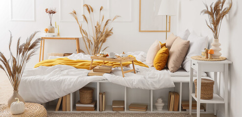 Interior of cozy bedroom with bed, shelving unit and vase of pampas grass