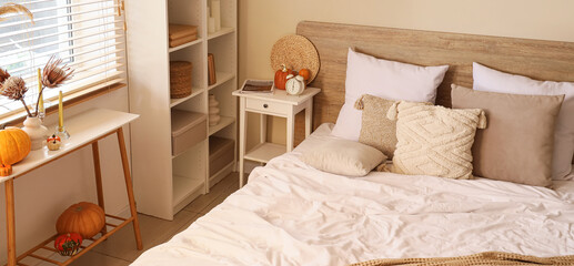Interior of modern bedroom with comfortable bed, pillows and pumpkins on bedside tables