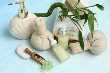 Set of spa supplies with bottles of cosmetic oil, sea salt, towel and herbal bags on light blue table