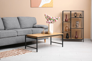 Vase with beautiful magnolia flowers and books on table near grey sofa in stylish living room © Pixel-Shot