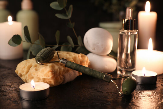 Composition with bath sponge, facial massage tool and burning candles on black grunge background, closeup
