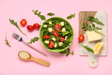 Bowl with tasty arugula salad and ingredients on pink background