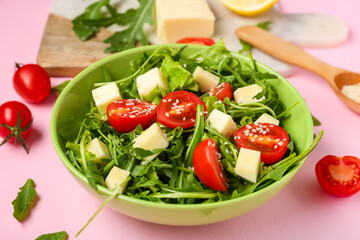 Bowl with tasty arugula salad on pink background, closeup