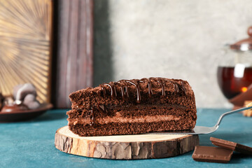 Wooden round slice with piece of tasty chocolate cake on blue table in kitchen, closeup