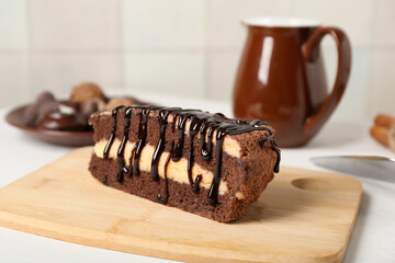 Piece of tasty chocolate cake on wooden cutting board on table in kitchen, closeup