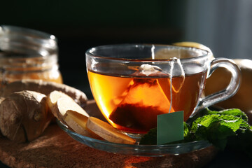 Cup of hot black tea with ginger root and mint leaves on table, closeup