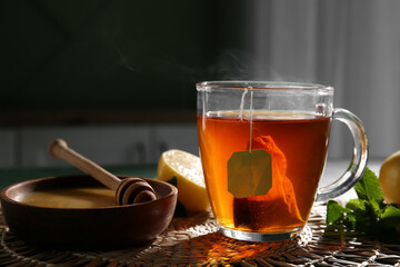 Cup of hot black tea with mint leaves and lemon on table, closeup