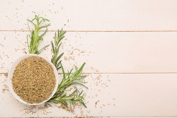 Composition with bowl of dried rosemary and fresh green twigs on white wooden background, closeup