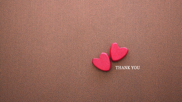 Top view, Two small red wooden hearts are placed together on a dark brown textured background, with the words "THANK YOU" in white text. The image symbolizes love, gratitude, and appreciation. - Powered by Adobe