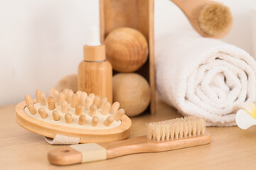 Massage body brushes, wooden balls and bottle of cosmetic product on table in room, closeup