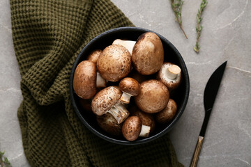 Black bowl with raw champignon mushrooms on grey grunge background, closeup