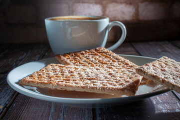 Golden cookies with sugar on top and a white cup with coffee or hot chocolate on a rustic wooden table with a brick wall background close up macro side view