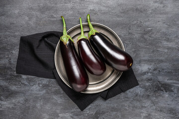 Plate with fresh eggplants on black grunge background